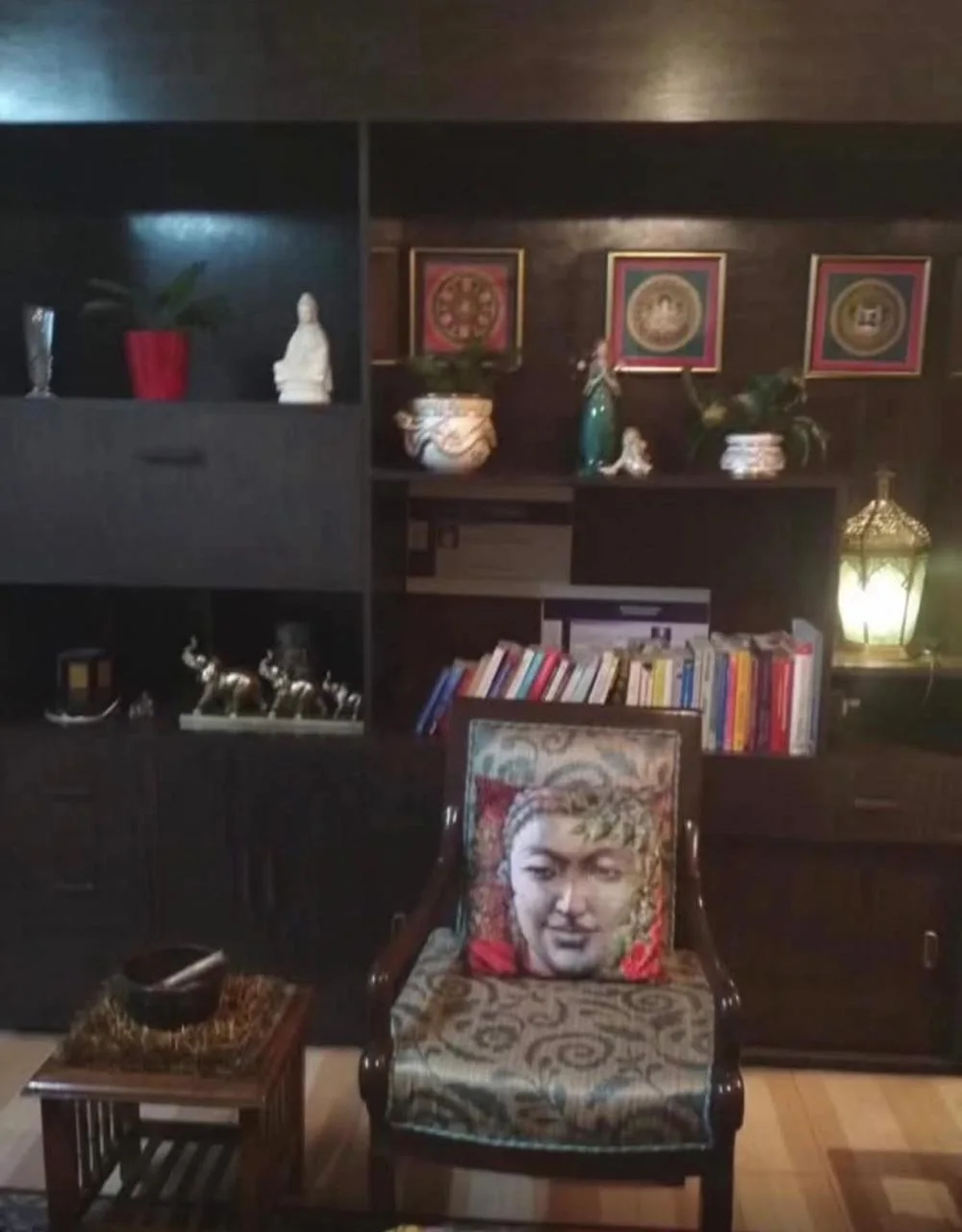 A healing room at the centre: a carved chair with a Buddha cushion, shelves of books, plants and Tibetan art
